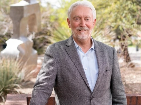 Horst Hahn wearing a gray blazer standing outside in a landscaped courtyard with a modern abstract sculpture and trees in the background.
