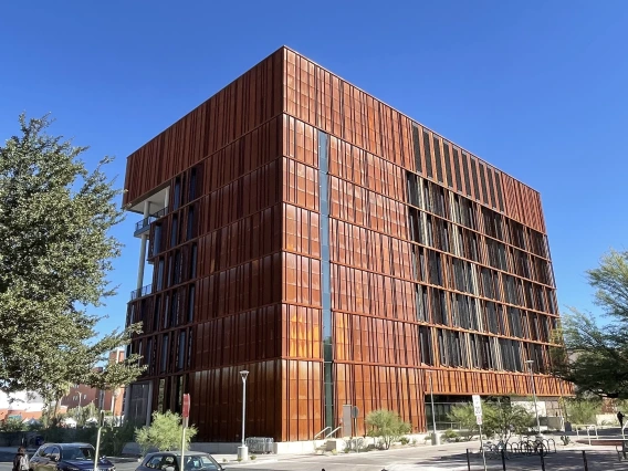 A large building sits between two trees under a clear, blue sky.