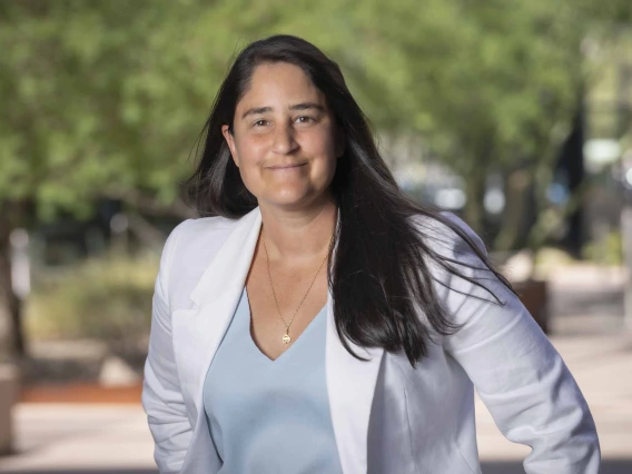 Portrait of Maya Kaelberer whereing a white blazer in an outdoor setting with trees in the background