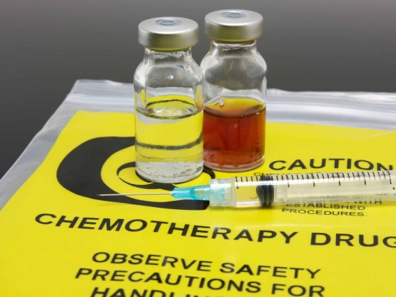 Two vials of liquid medication and a syringe on an empty yellow bag with black text “chemotherapy drug, observe safety precautions”