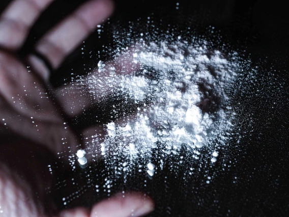 Accumulation of white powder placed on a black background, with a man’s hand mirrored behind the powder