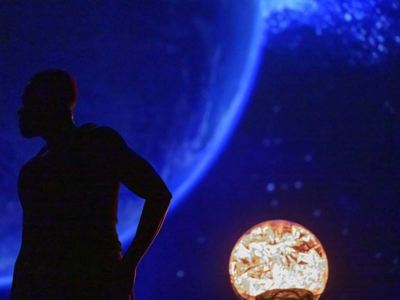 A dancer stands in silhouette in front of an image of space