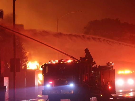 Firefighter on top of fire truck using hose to spray water on burning homes