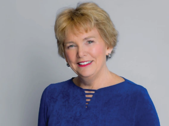 A woman with short hair in a blue top smiles for a portrait.