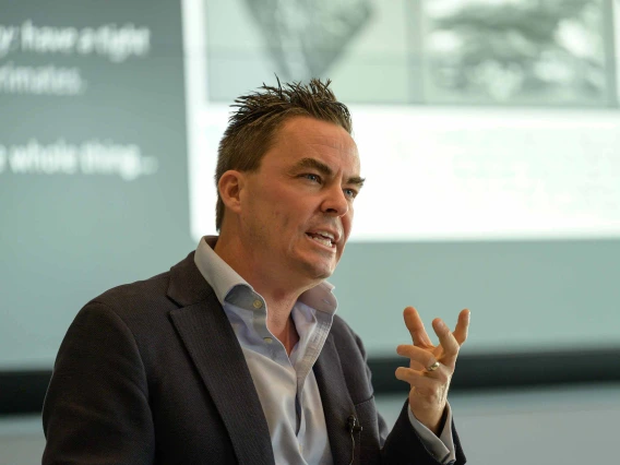 A man is talking intensely while a projection screen in the background 