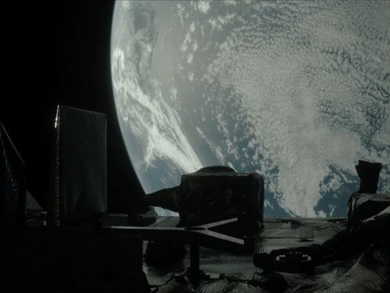 Earth fills most of the image, a moody blue globe mostly covered with tiny blueish white clouds like carpet pile or sheep’s wool. In the foreground, the instrument panel is dark enough to be nearly in silhouette, like a city skyline. A tall thin rectangle juts up from the left side of the panel, like a tall building, which is part of the SamCam. In the center, a shorter, squatter polygon shape is the OLA instrument. A slightly lighter colored Y shape lays on its side in front of the OLA.