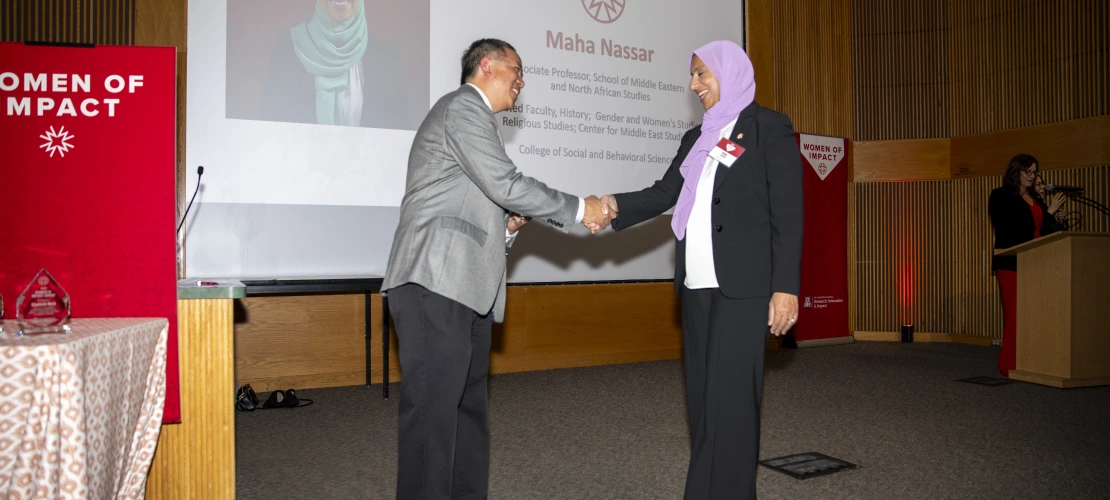 Two individuals shake hands in front of a projector screen.