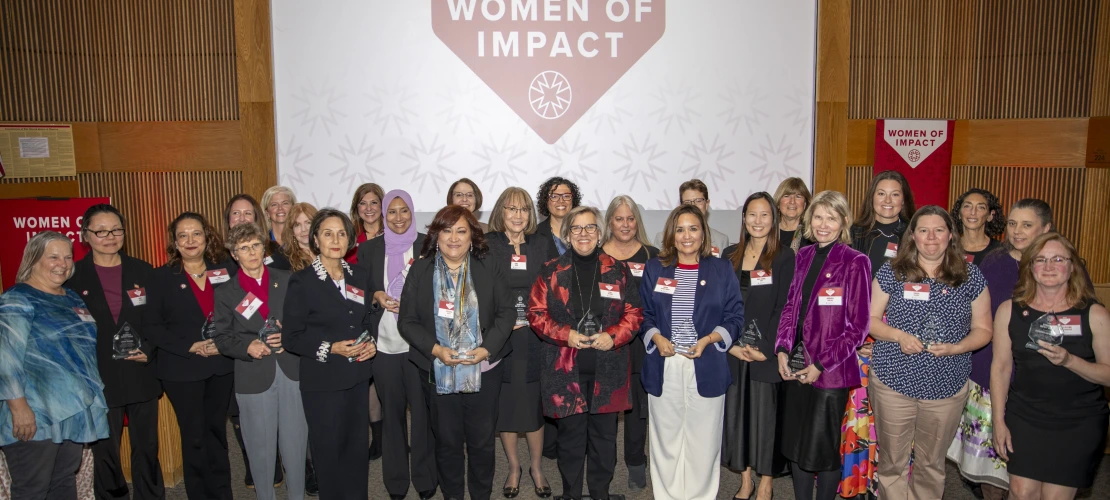 A group of women holding their awards pose for a photo in front of a projector screen.