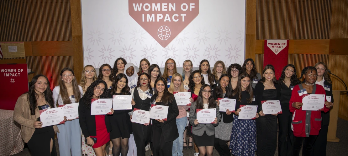 A group of young women holding their awards pose for a photo in front of a projector screen.