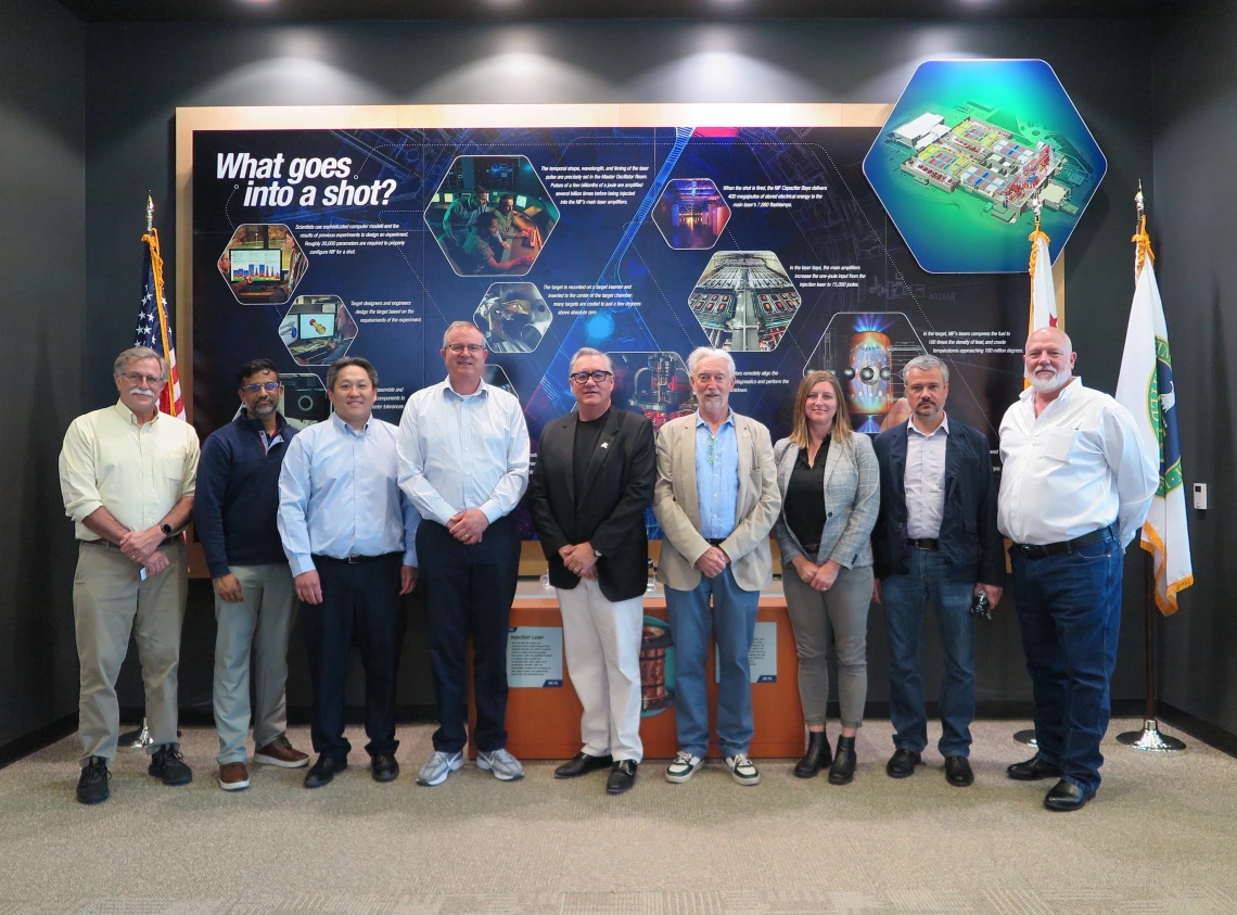 A line of people pose for a photo in front of an informational backdrop related to fusion energy.