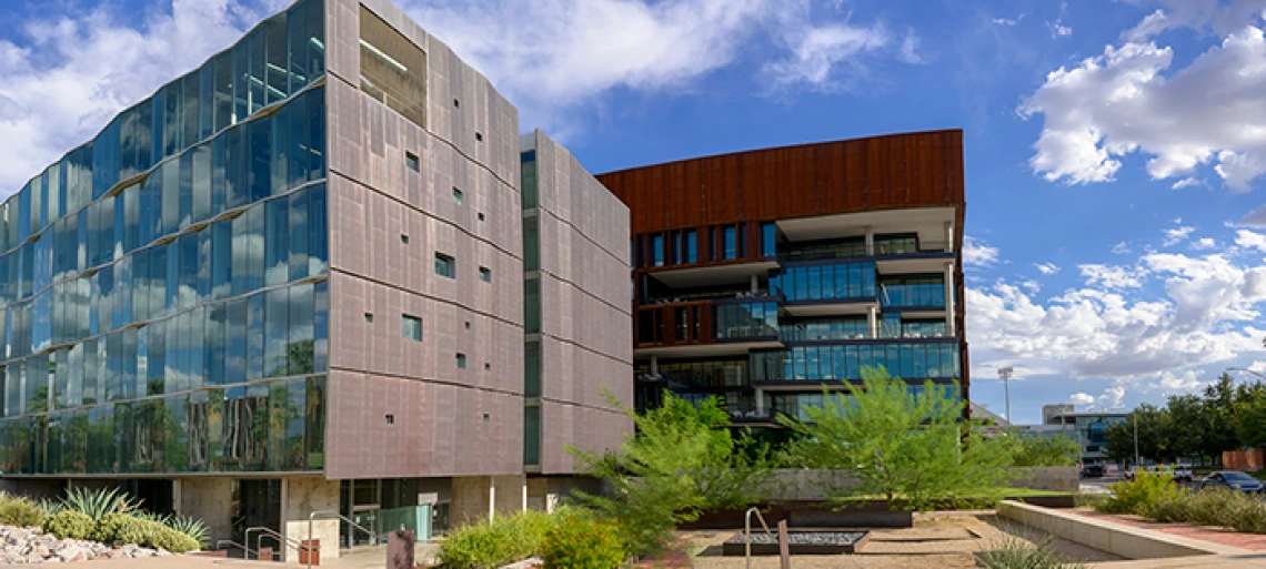 A wide angle photo of the Grand Challenges Research Building taken mid-afternoon in front of a bright blue sky with scattered clouds