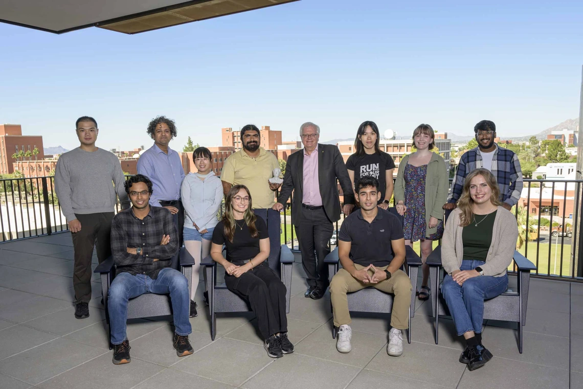 Twelve people, most of whom are graduate students, sit and stand in a group on a balcony.