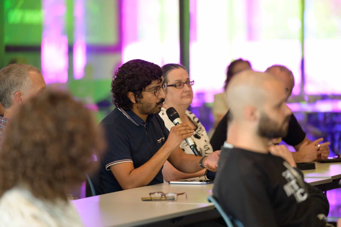A man in an audience holds a microphone as he asks the presenter a question. 