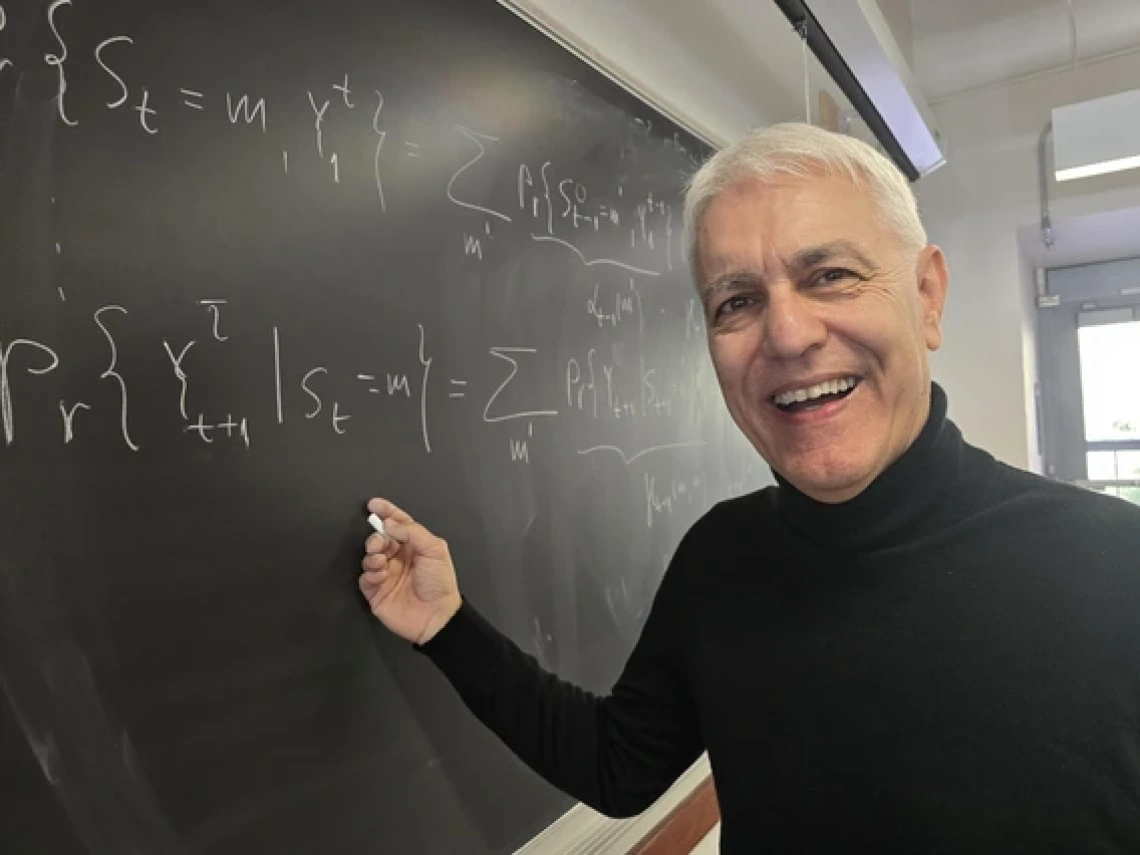 A professor wearing a black shirt writes on a chalkboard