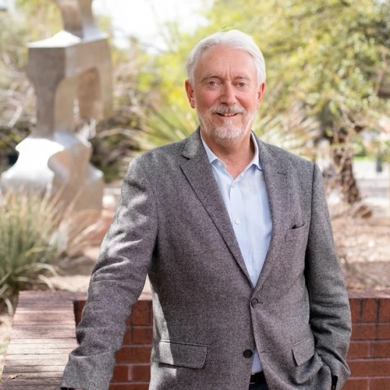 Horst Hahn wearing a gray blazer standing outside in a landscaped courtyard with a modern abstract sculpture and trees in the background.