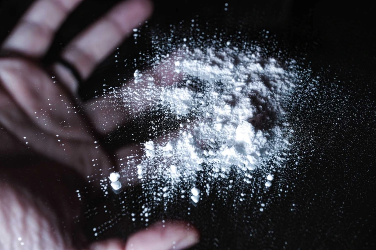 Accumulation of white powder placed on a black background, with a man’s hand mirrored behind the powder