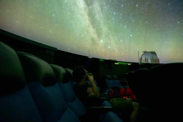 Person sitting in dark planetarium watching video show projected on ceiling 