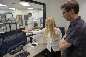 Two people stand in a research lab looking at data on a computer monitor